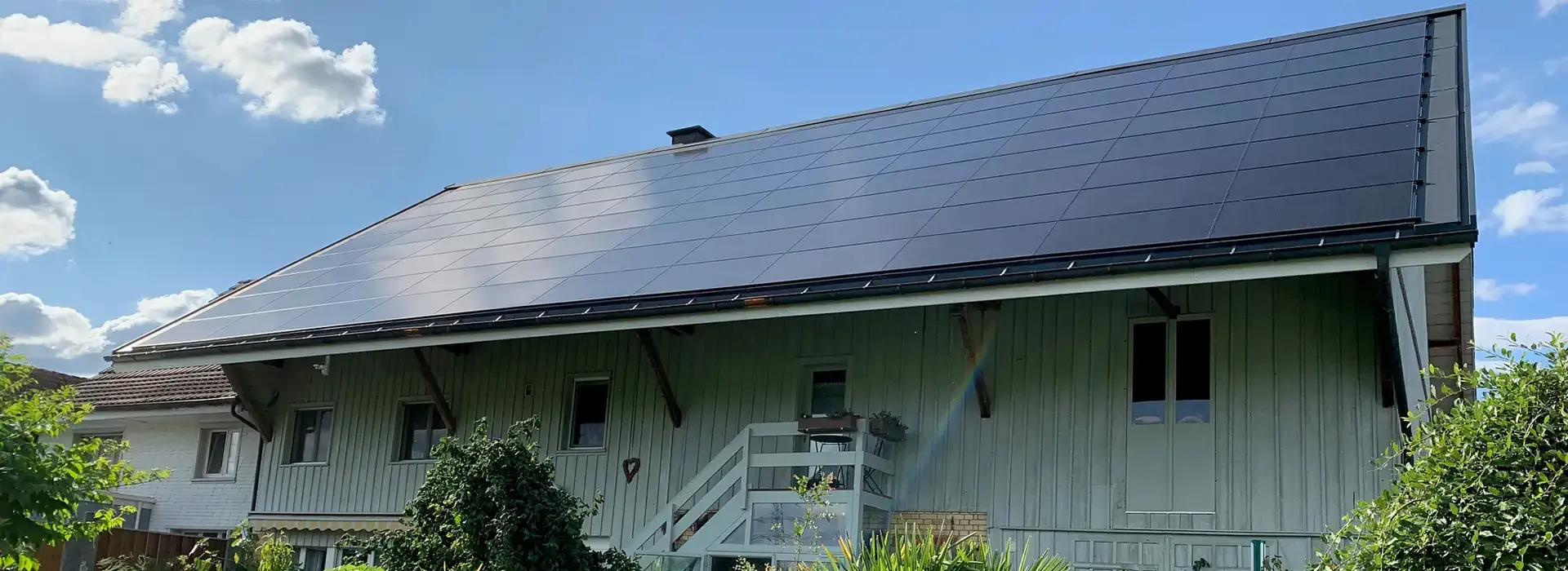 türrkises haus mit solarpanels auf dem dach und grünem garten